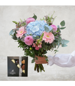 Smuk blomsterbuket med lyseblå hortensia i midten omgivet af lyserøde blomster.